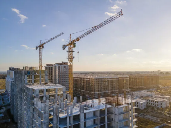Cranes on the construction site surrounded by new real estates. Scenic aerial photo of growing city districts