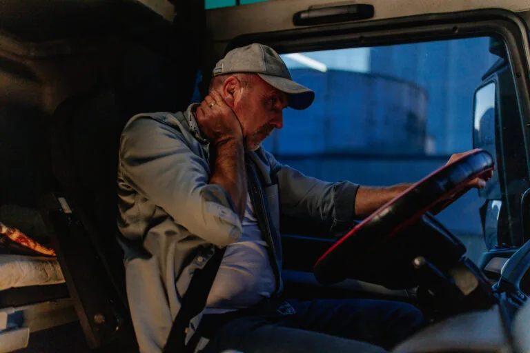Exhausted truck driver feeling tired and massaging neck while driving his truck.