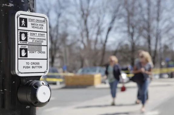 Close up, rack focus of a crosswalk sign and button. A red, blurred car drives by.