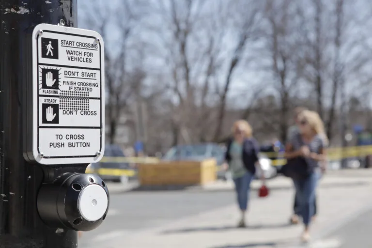 Close up, rack focus of a crosswalk sign and button. A red, blurred car drives by.