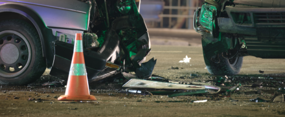 Two cars with severe front-end damage after a nighttime collision with a traffic cone nearby
